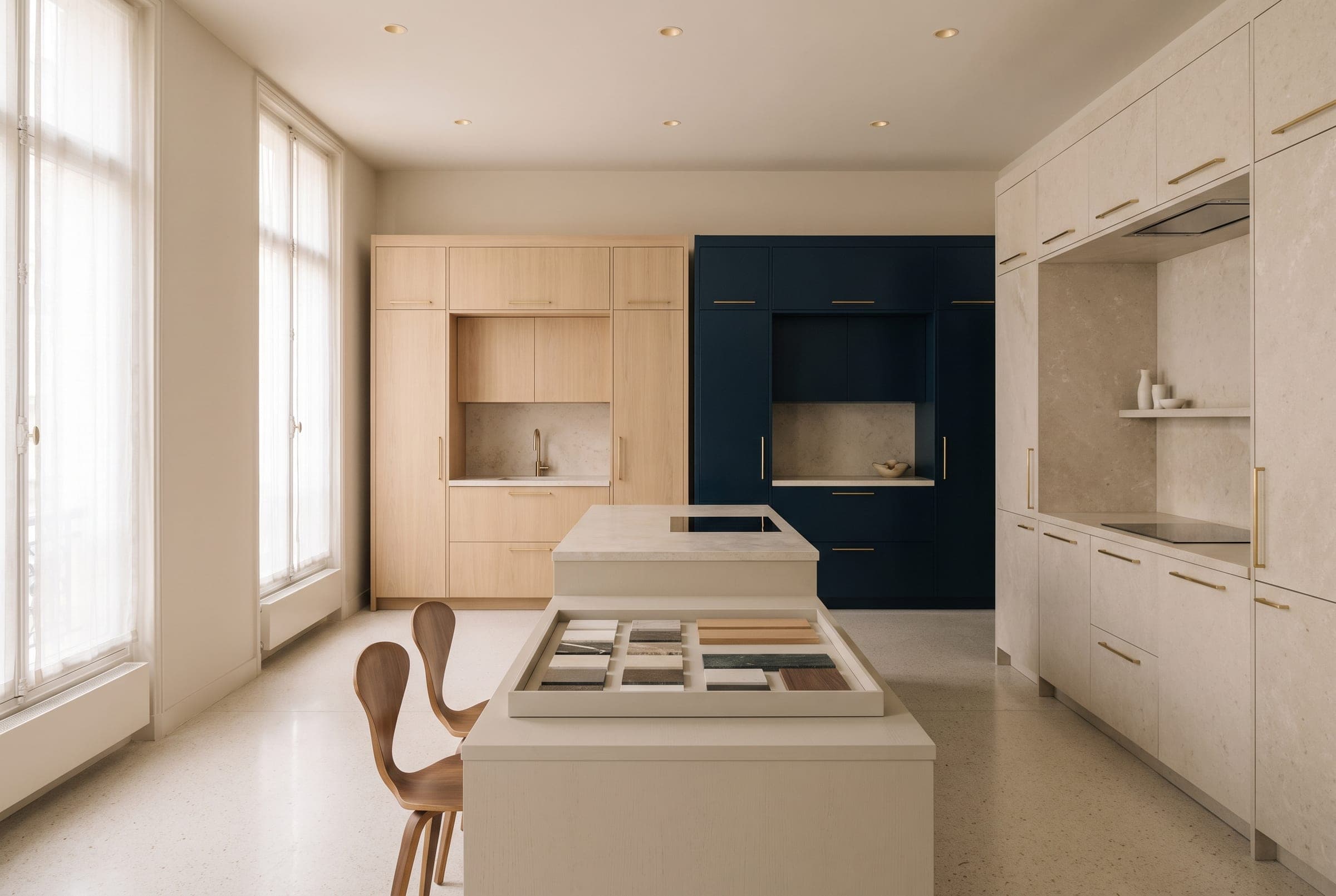 Le showroom du 66 avenue des Champs-Élysées : implantations de cuisines sur mesure en chêne et laque bleu nuit, îlot central servant de table de conseil, échantillons de pierre et de bois.
